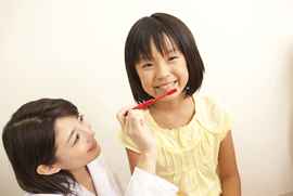 笑顔の子供が歯科衛生士と歯磨き訓練を受けている写真